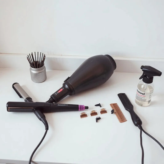 A curated set of professional hair styling tools on a clean salon counter, including dryer, iron, clips, and combs.
