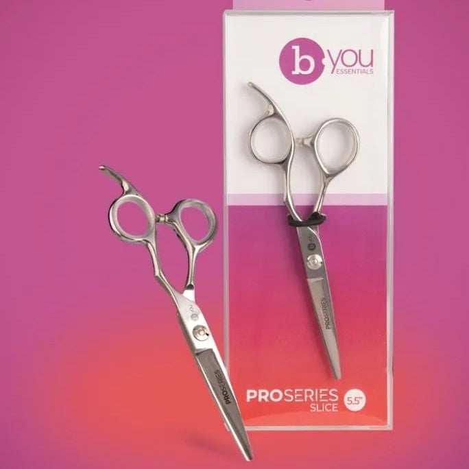 B You Professional ProSeries Slice scissors shown both outside of their packaging and inside its clear retail box, set against a pink and orange gradient background.